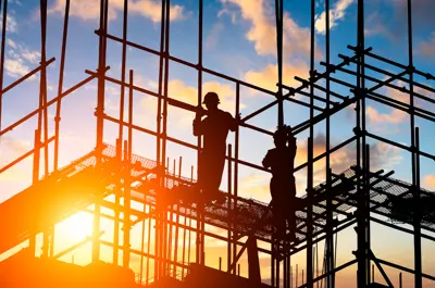 A worker on scaffolding against the setting sun.